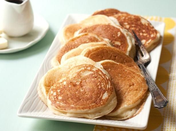 several pancakes on a white plate with syrup and coffee in the background that says vanilla greek yogurt protein pancakes