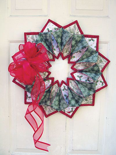 a christmas wreath hanging on a door with red ribbon and bow attached to the front