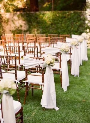 rows of wooden chairs with white sashes and flowers on them are set up for an outdoor ceremony