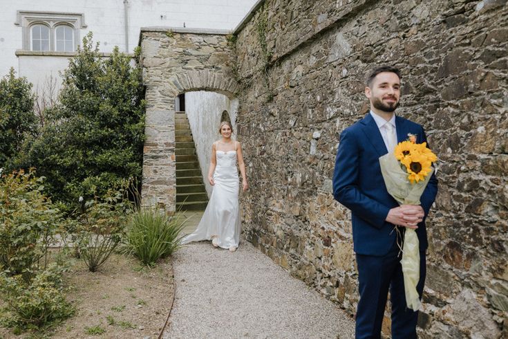 a man in a suit and tie holding a sunflower bouquet next to a woman in a white dress