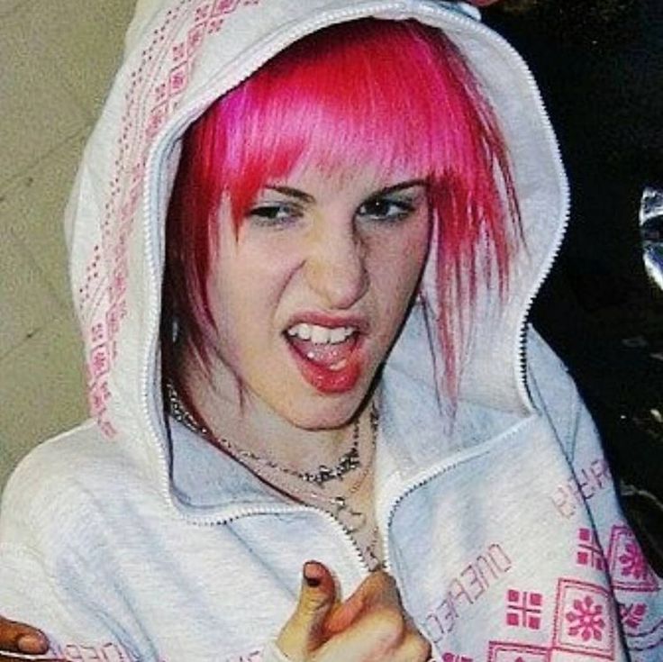 a young woman with pink hair and piercings on her finger, wearing a white hoodie