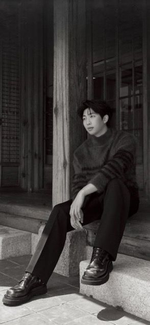 black and white photograph of a young man sitting on the steps with his legs crossed