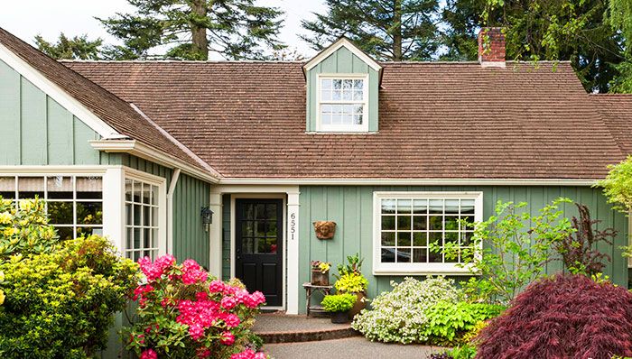 a green house with lots of flowers in front of it and trees around the yard