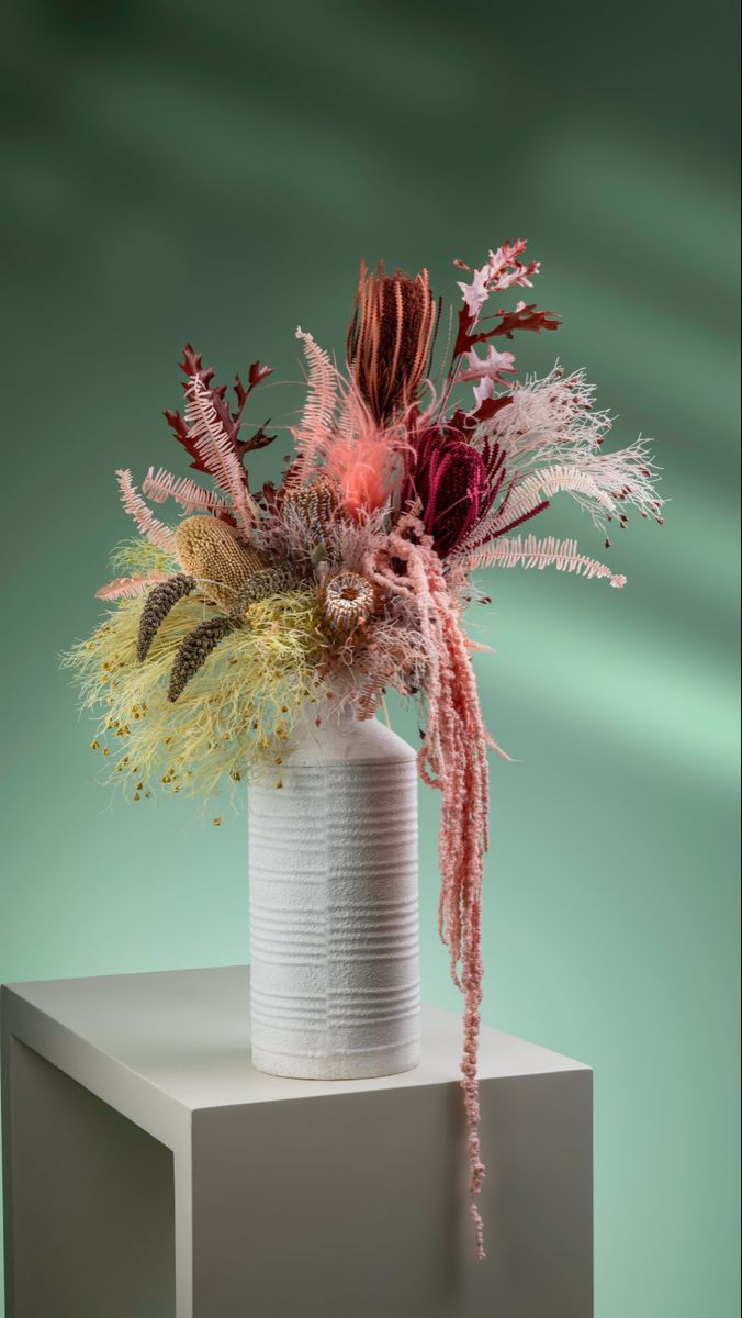 a white vase filled with flowers on top of a table next to a green wall