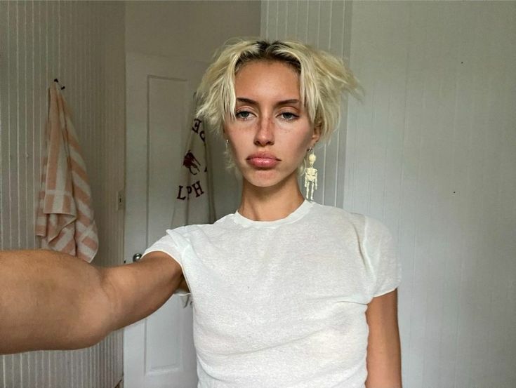 a woman is getting her hair styled by a man with blonde hair in a white t - shirt