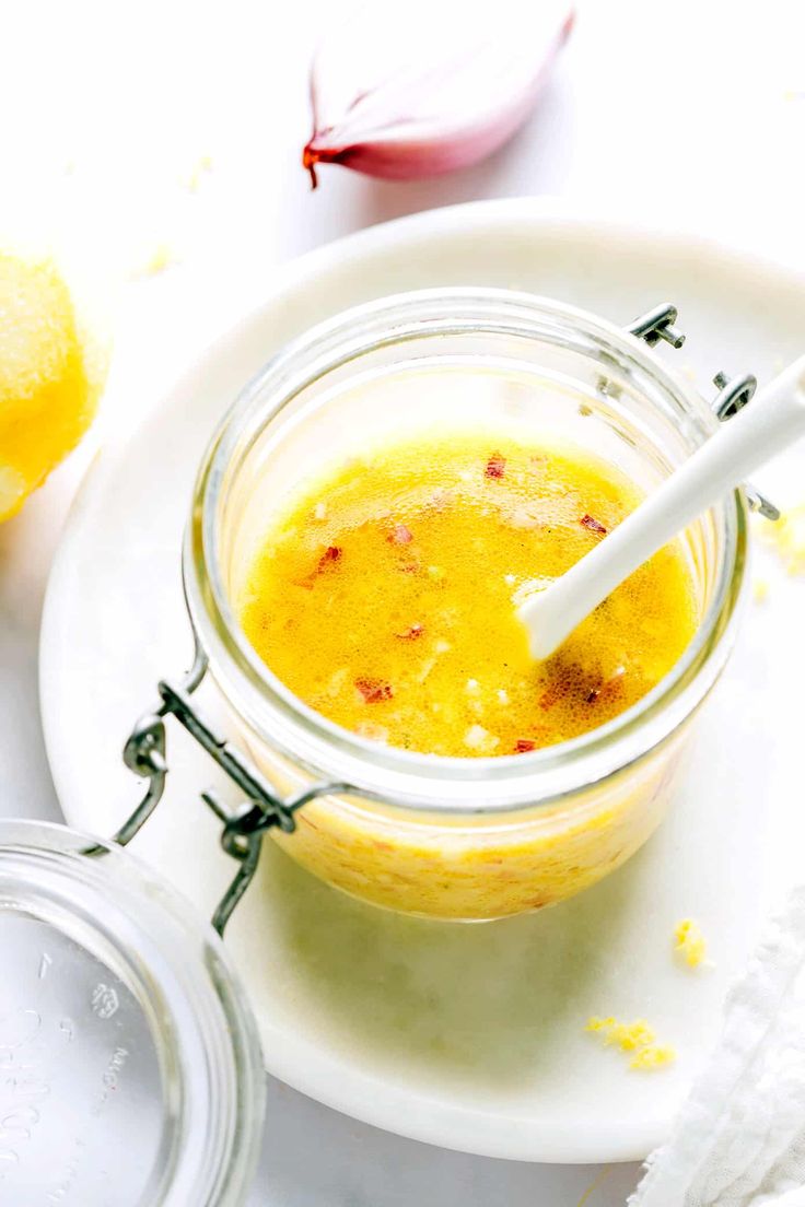 a glass jar filled with yellow liquid next to sliced lemons and garlic on a white plate