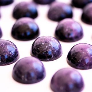 some very pretty purple rocks on a white surface with water droplets all over them and the stones are shiny