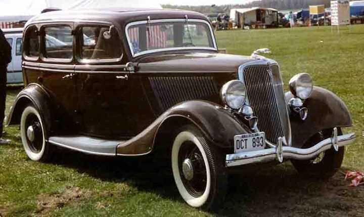 an old car is parked on the grass near other cars and people standing around it