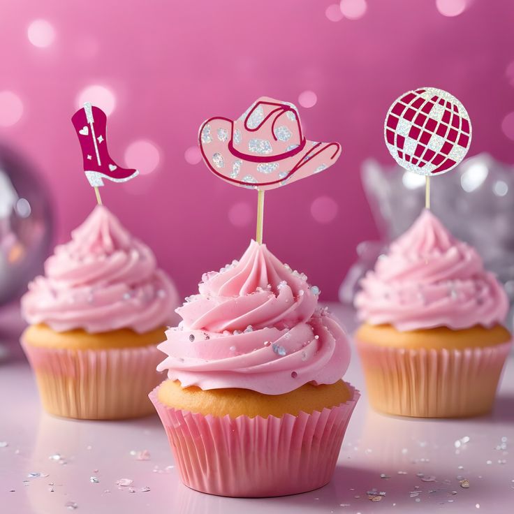 three cupcakes with pink frosting and decorations on top, one has a cowboy hat