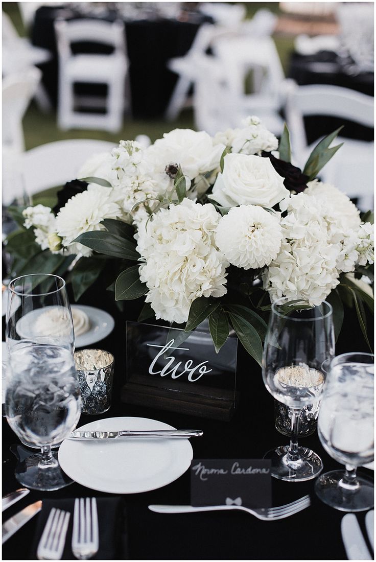 the centerpieces on this table are white flowers and black napkins with silverware