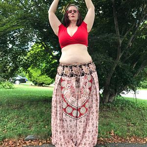 a woman standing in the grass with her hands up to her head and wearing a red top