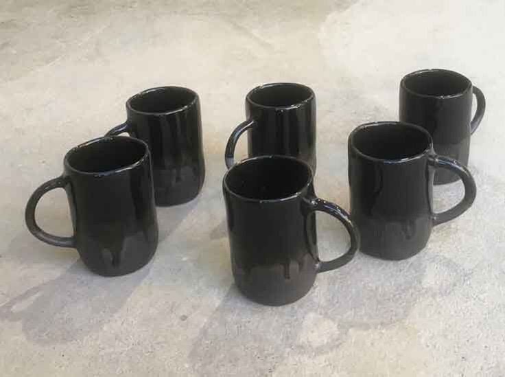 five black coffee mugs are lined up on the floor