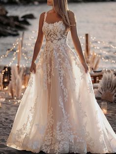 a woman in a wedding dress is standing on the beach with candles and lights behind her