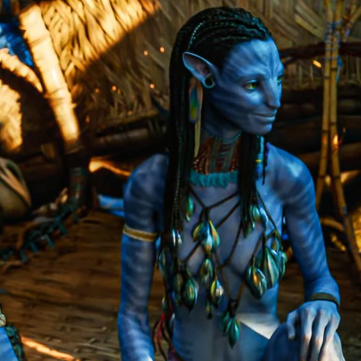 a woman with blue paint on her face and body sitting in front of a hut