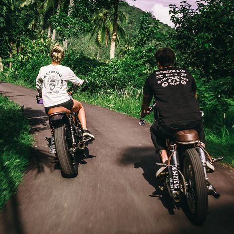 two people riding motorcycles down a road next to trees and bushes on either side of them