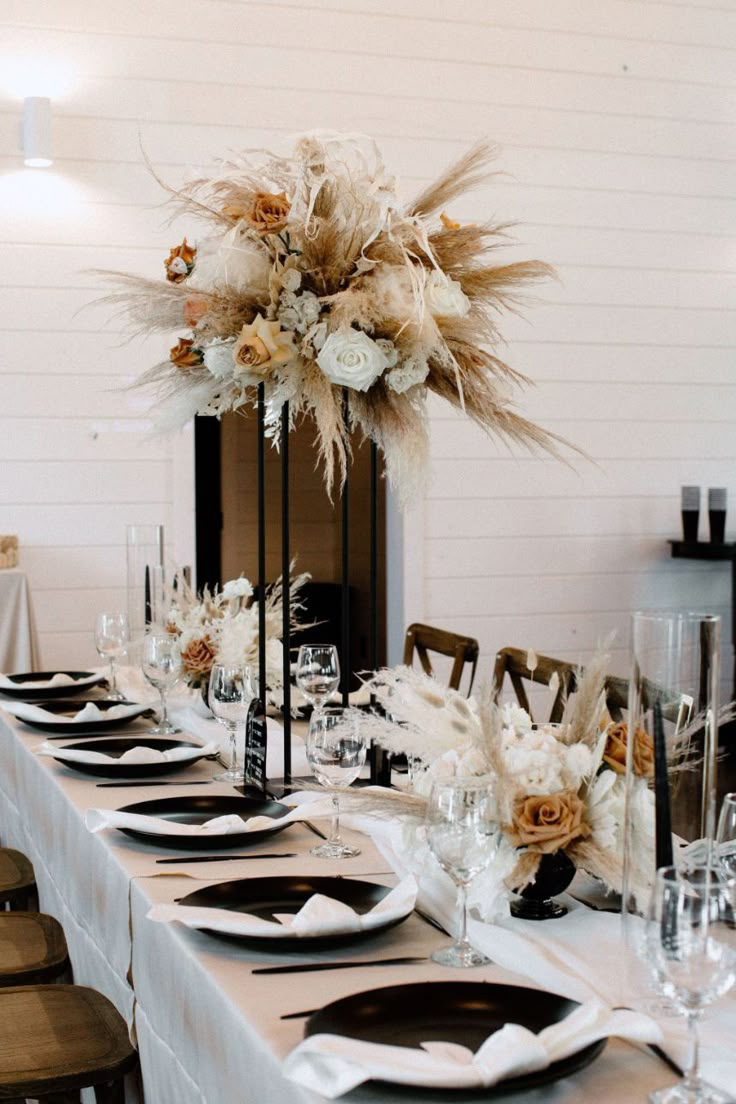 a table set with black and white place settings, tall centerpieces and flowers