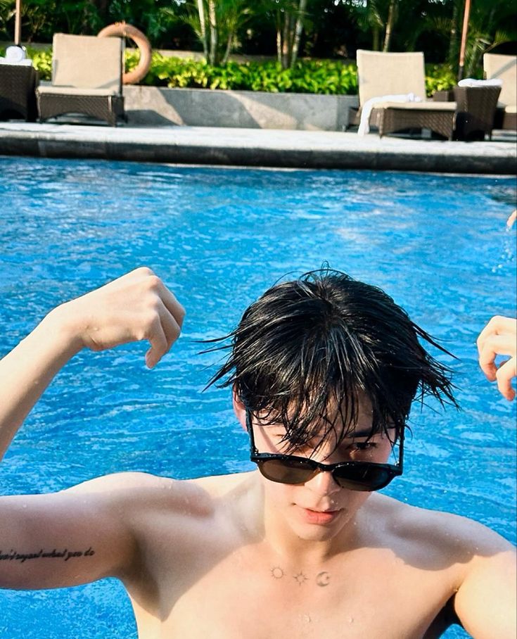 a shirtless man standing in front of a swimming pool with his arm raised up