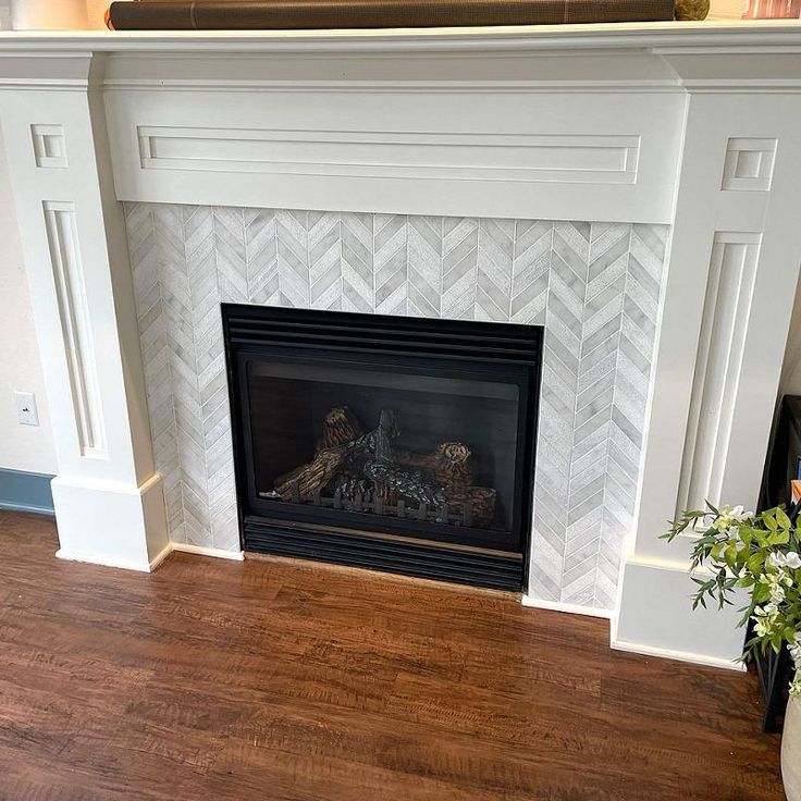 a white fireplace with wood flooring in a living room next to a potted plant