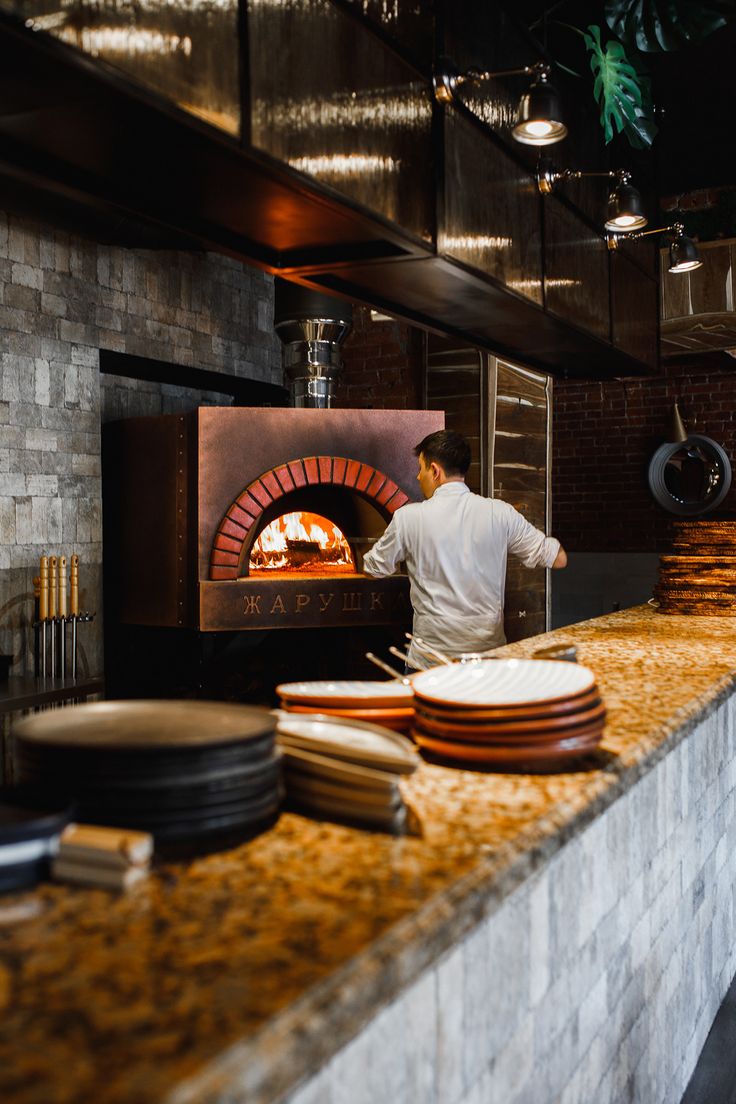 a man standing in front of an oven with pizzas on the counter and plates