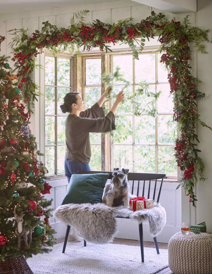 a woman standing in front of a christmas tree with her dog sitting on a bench