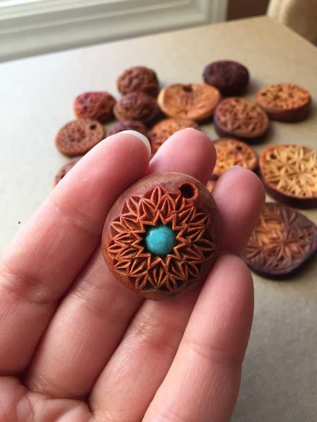 a hand holding a small bead in front of some other beads on a table