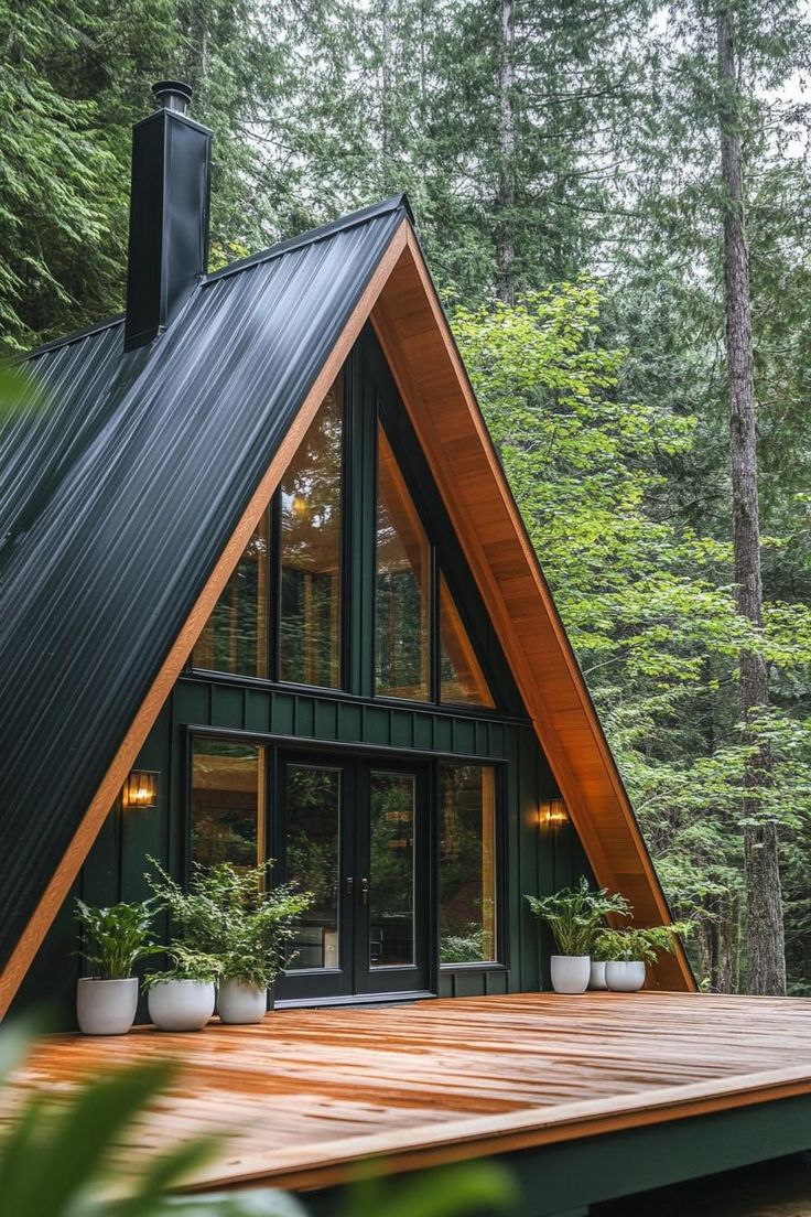 a - frame cabin in the woods with wood decking and potted plants on the porch