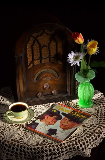 a table topped with a cup of coffee next to a magazine and a vase filled with flowers