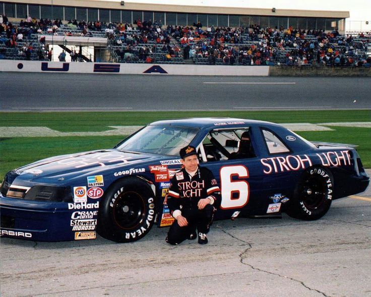 a man sitting next to a racing car on top of a race track