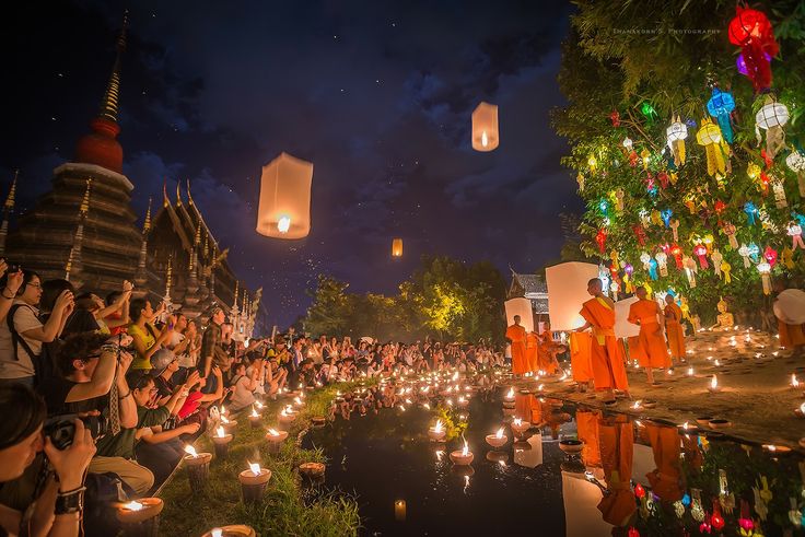 many people are holding candles in front of the water and lanterns flying above them at night