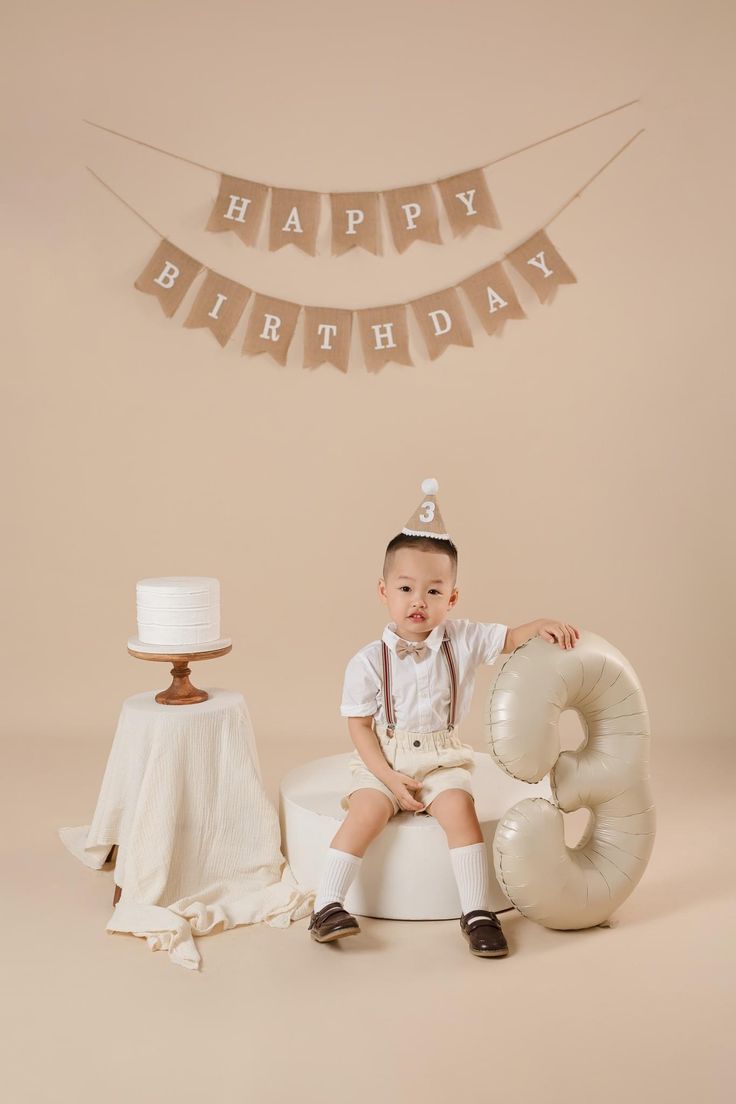 a little boy sitting on top of a cake in front of a happy birthday banner