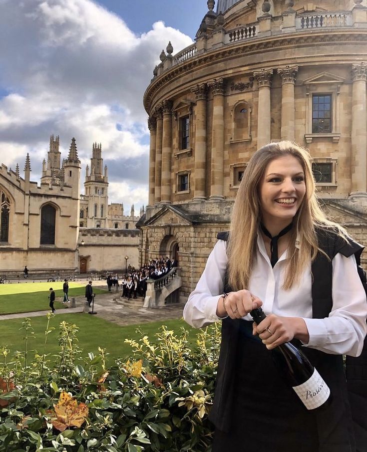 a woman standing in front of a building holding a wine bottle