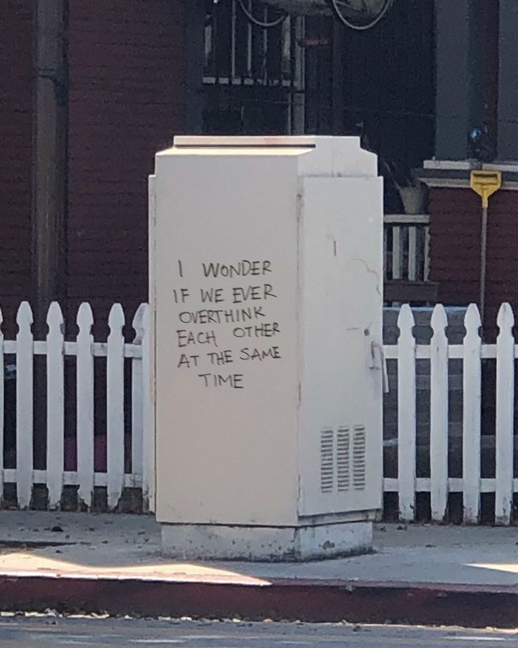 a white box sitting on the side of a road next to a white picket fence