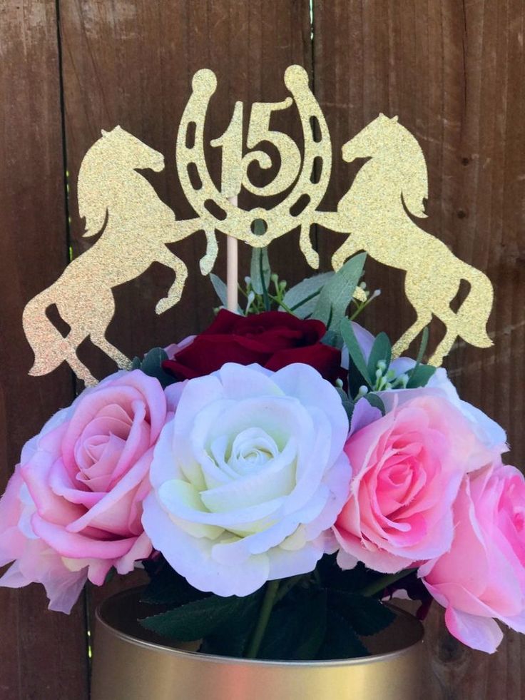 a vase filled with pink and white roses on top of a table next to a wooden fence