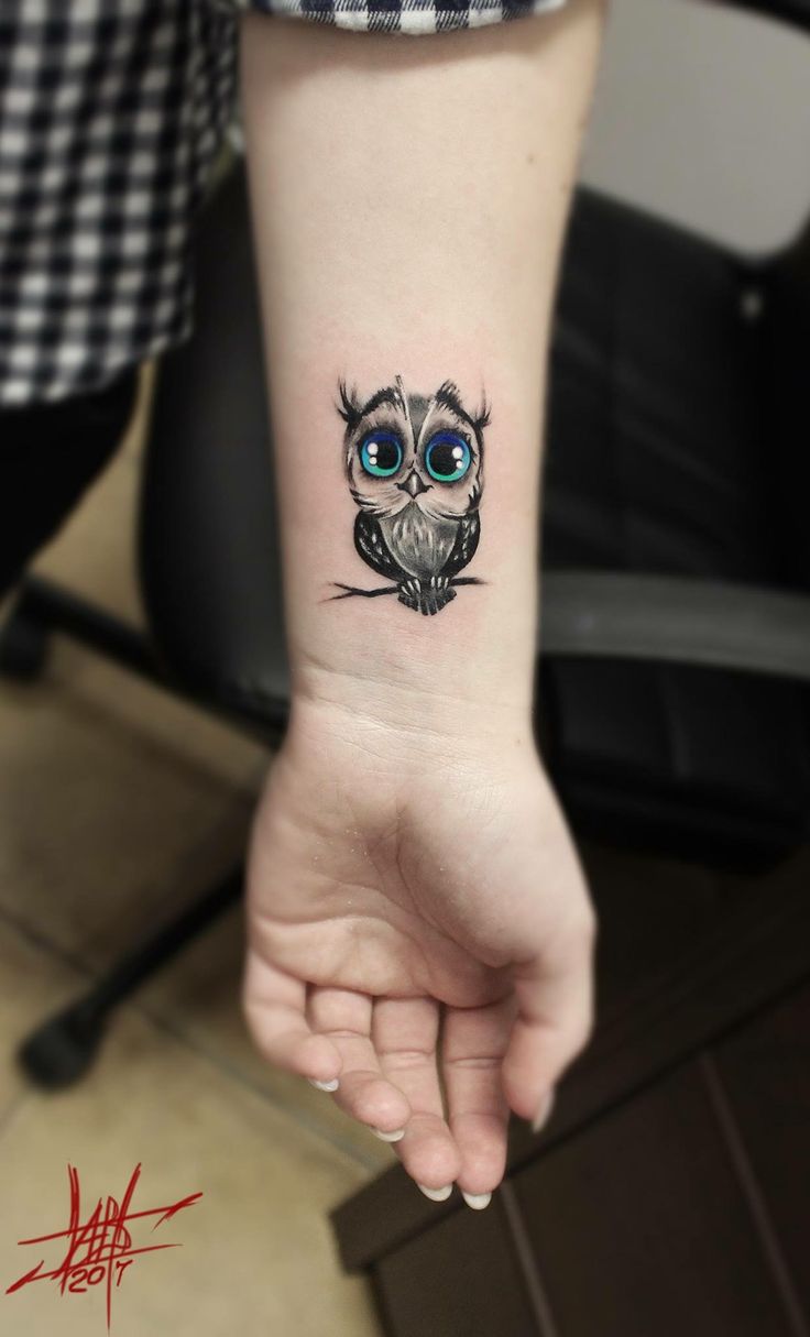 a small owl tattoo on the left inner forearm and wristband, with blue eyes