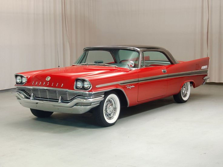 an old red car is parked in a room with drapes on the windows and curtains behind it