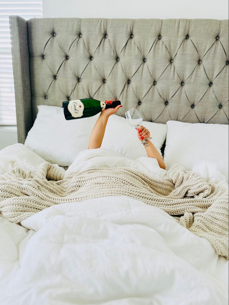 a woman laying in bed with her feet up on the pillow and holding two champagne bottles