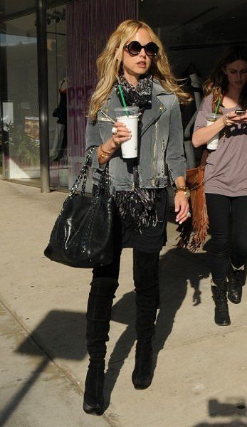 a woman walking down the street carrying a black purse and holding a coffee in her hand