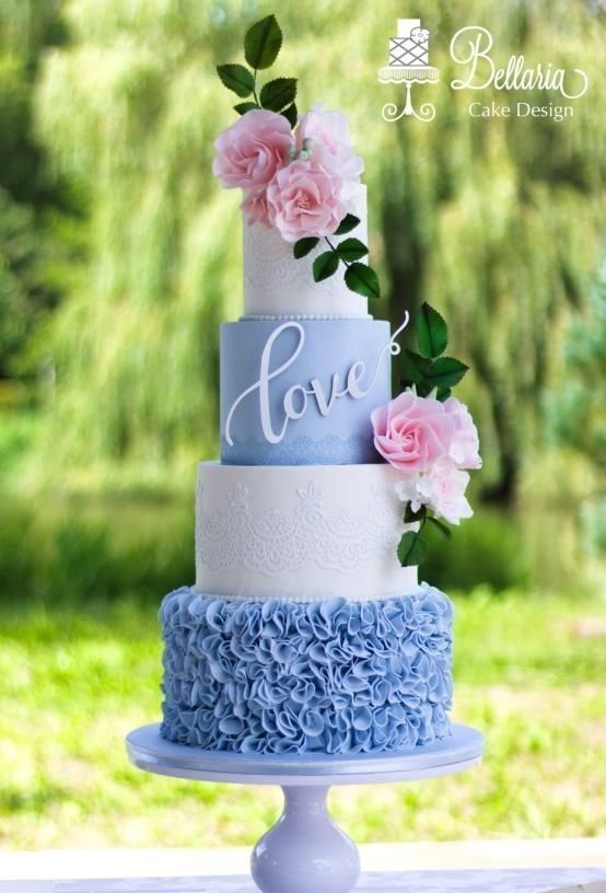 a blue and white wedding cake with pink flowers on the top is sitting on a table