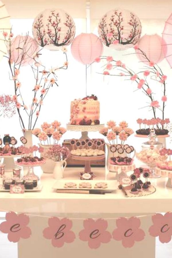 a table topped with cakes and desserts covered in frosting under pink paper lanterns