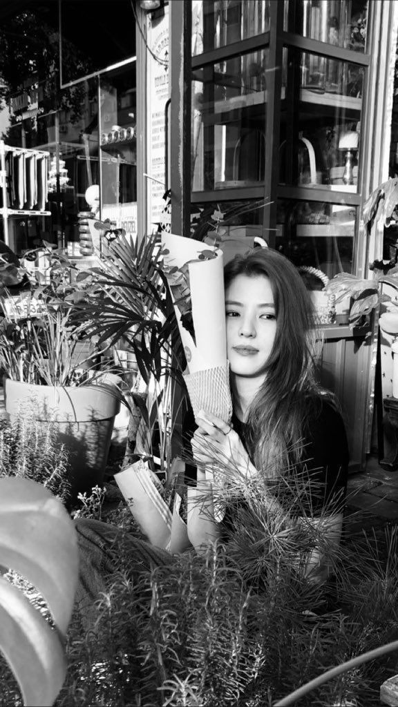 a black and white photo of a woman in front of some plants with her hand on the planter