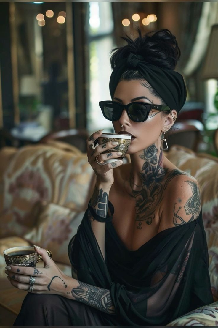 a woman with tattoos on her arm drinking from a cup while sitting on a couch