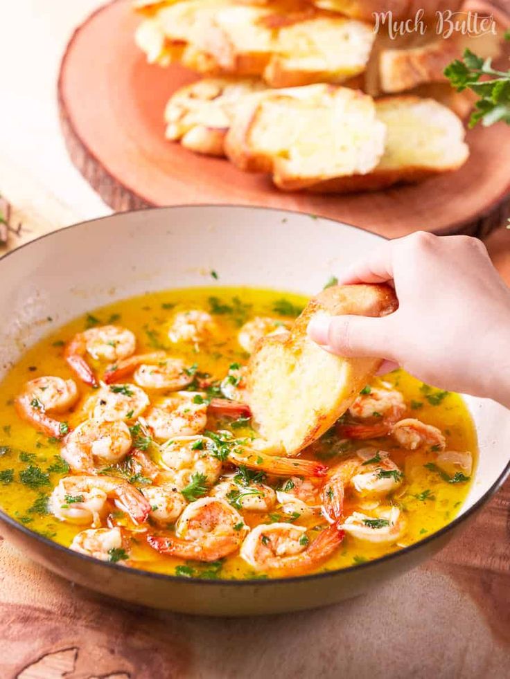 a person dipping bread into a bowl of shrimp soup