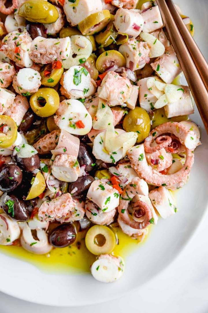 a white plate topped with shrimp and olives next to chopsticks on a table