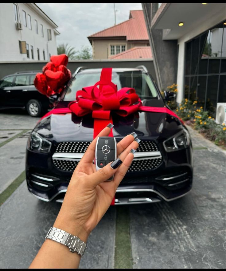 a hand holding a car key in front of a black sports car with red bows on it