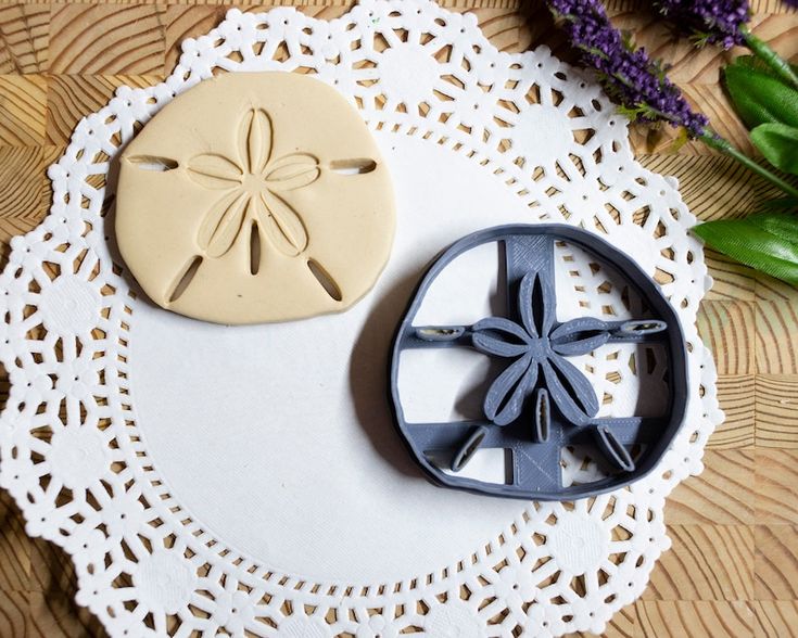 two cookie cutters sitting on top of a white doily next to purple flowers