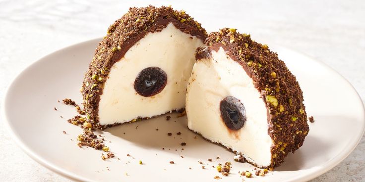 a white plate topped with a cut in half cheesecake covered in chocolate and cherries