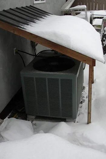 an air conditioner sitting in the snow next to a building with a wooden roof