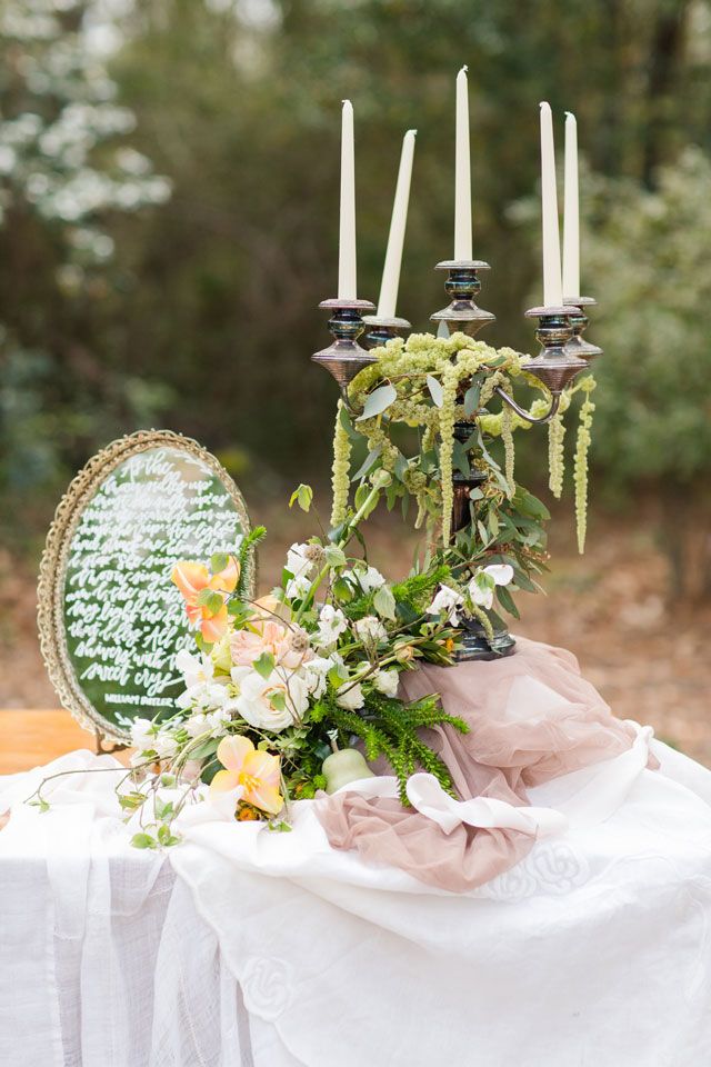 a table with candles and flowers on it next to a mirror in the middle of the forest