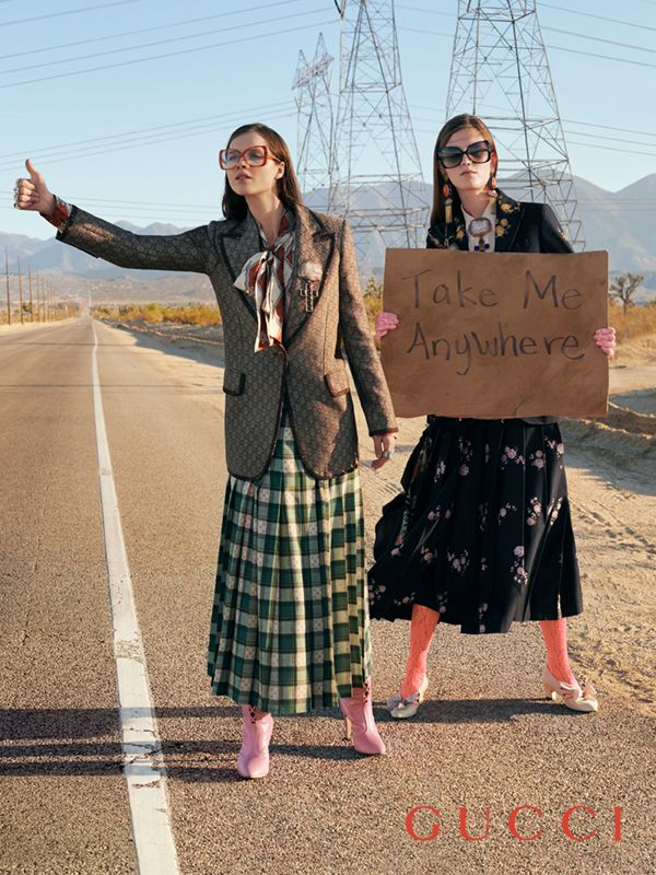 two women standing on the side of an empty road holding up a sign that says take me anywhere