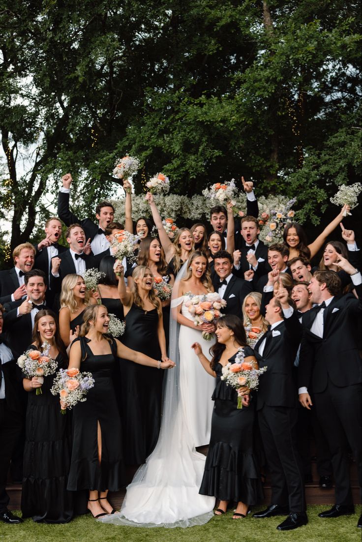 a large group of people in formal wear posing for a photo with their hands up